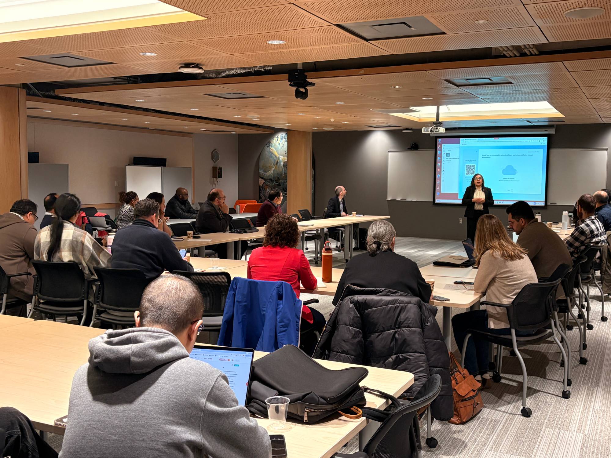 Wide view of the workshop room with participants seated at tables facing the presentation screen.